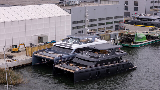 Aerial view of two luxury catamarans docked at a shipyard with industrial buildings in the background in Gdansk, Poland.