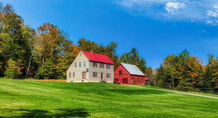 Charming farmhouse and red barn in a rural autumn landscape with green lawn and blue sky © KANGWEN