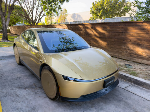 Dallas, Texas, USA - October 15th, 2026: Front view of gold Tesla Cybercab prototype parked in lot outside Tesla service center building