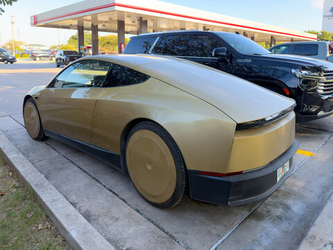 Dallas, Texas, USA - October 15th, 2026: Gold Tesla Cybercab prototype parked beside SUV at service center parking lot near gas station background
