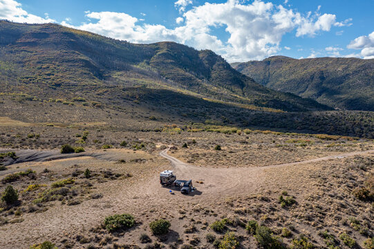 Aerial view of two vehicles in dispersed camping site in Colorado backcountry under sunny autumn cloudscape.