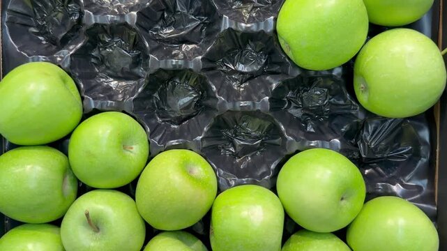 Green granny smith apples in black plastic packaging tray inside grocery store market. Fresh organic fruit, healthy eating, autumn harvest season, retail counter display, raw food gastronomy product.