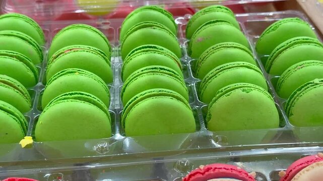 Green macaron cookies in rows inside plastic packaging tray at confectionery store. Sweet delicate desserts, french baking, pastry shop showcase,  gourmet confection product.