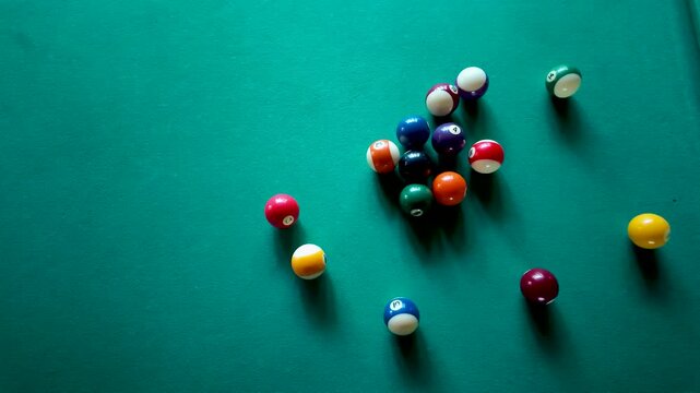 Overhead view of pool cue ball breaking racked billiard balls on green felt table