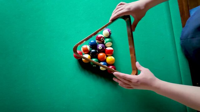 Caucasian player setting up colorful billiard balls with wooden triangle rack