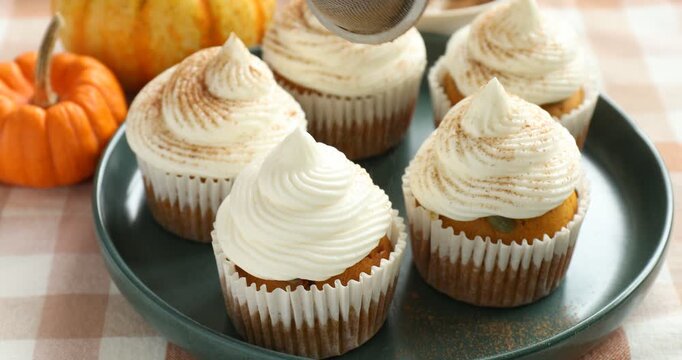 Woman sprinkling cinnamon onto delicious pumpkin cupcake at table, closeup