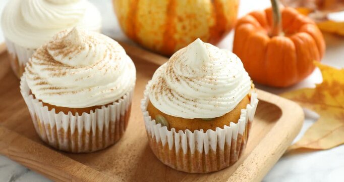 Sprinkling cinnamon onto delicious pumpkin cupcake at white marble table, closeup