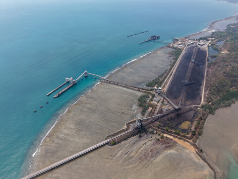 Aerial view of Sarang Tiung coal terminal with conveyor belts, stockpiles, and a jetty extending into the sea in Pulau Laut Utara, South Kalimantan, Indonesia.