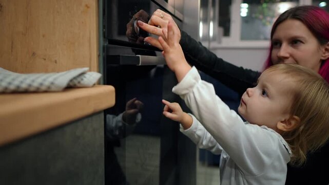Mother and her little daughter are turning on the electric cooker to heat it before baking filmed in slow motion. Young adult Caucasian lady and her little child engaged in process of preparing meal