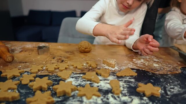 A little girl and her family bake homemade cookies together. They knead the dough and use cutters to shape star shaped biscuits on the table. Warm moments of love and the magic of the holiday season.