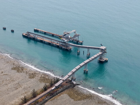 Aerial view of Sarang Tiung coal loading terminal with industrial conveyor belts extending into the sea along the rocky coastline of Pulau Laut Utara, South Kalimantan, Indonesia.