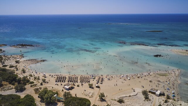 Overtourism, sandy beach with many parasols and people enjoying the clear blue sea. The sky is cloudless, Elafonissi, lagoon, south-west tip of Crete, Crete, Greek islands, Greece
