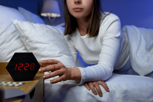 Insomnia and sleep disorder, woman waking up at night checking digital alarm clock with stress and anxiety in bedroom at home