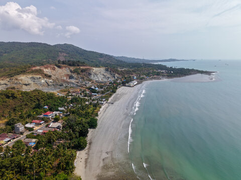 Aerial view of Gedambaan beach with lush tropical vegetation, coastal hills, and a nearby residential area in Pulau Laut Utara, South Kalimantan, Indonesia.