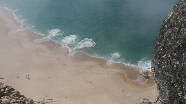 Fog rolling in and ocean waves below from high over rocky cliff view of Praia do Norte in Nazar&eacute; Portugal