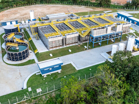 Aerial view of a modern water treatment plant featuring modular stainless steel tanks, yellow structural frames, and circular sedimentation basins set within a landscaped facility.