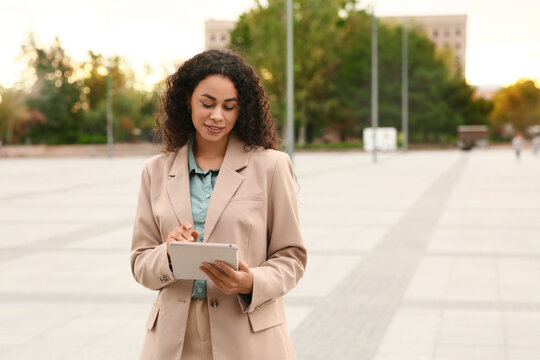 Remote work and digital nomad lifestyle, young woman using a tablet computer for business communication while standing in an urban outdoor city plaza