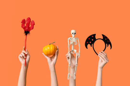 Halloween party celebration and festive fun, hands holding devil trident pumpkin skeleton and bat wings accessories on a bright orange background
