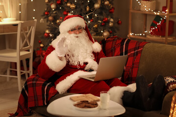 Santa Claus video calling on laptop, remote communication and holiday greetings concept, festive home interior with christmas tree and cookies © Pixel-Shot