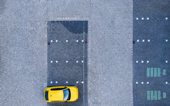 Aerial view of a yellow car parked in a paved lot with herringbone pattern bricks in The Netherlands.