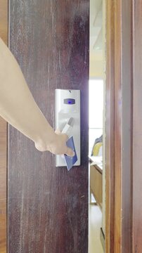 A person tapping an RFID key card on a modern electronic smart door lock reader, turning the handle, and entering a hotel room.