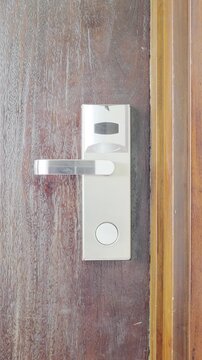 A person tapping an RFID key card on a modern electronic smart door lock reader, turning the handle, and entering a hotel room.