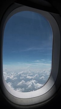 View through an airplane window showing a thick white cloud layer beneath a clear blue sky during a daytime flight