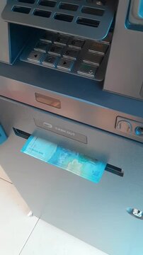 hand withdraws cash from ATM machine. User interacts with banking machine. Modern payment solution in public space. Urban setting for daily transactions. vertical.