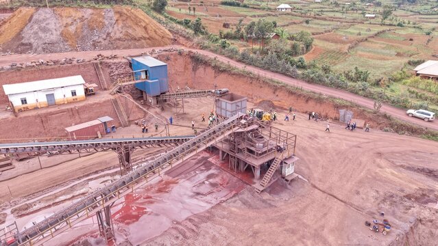 Aerial view of a mining site with conveyor belts, heavy machinery, and workers in a rural landscape in Kabale, Western Region, Uganda.