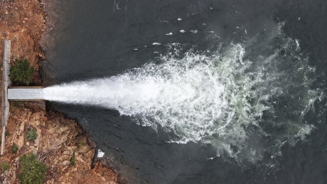 Aerial view of water rushing from a concrete spillway into Marys Lake, with rocky terrain and vegetation along the shoreline in Estes Park, Colorado, United States.