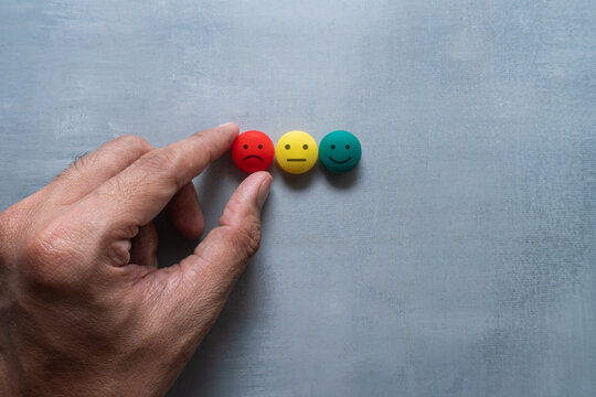 Hand selecting a red unhappy face beside neutral and smiling emotion icons. Negative feedback, dissatisfaction, mood assessment, complaints