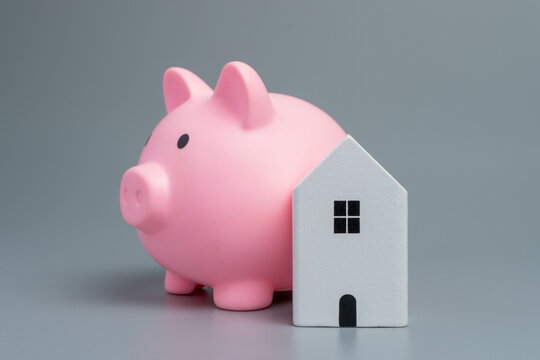 Piggy bank and miniature house on a gray background. Home savings, mortgage planning, property investment, housing costs, down payments concept.