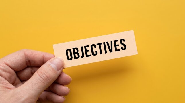 Hand holding card with word objectives against bright background with Hand displays card labeled objectives solid yellow backdrop communication