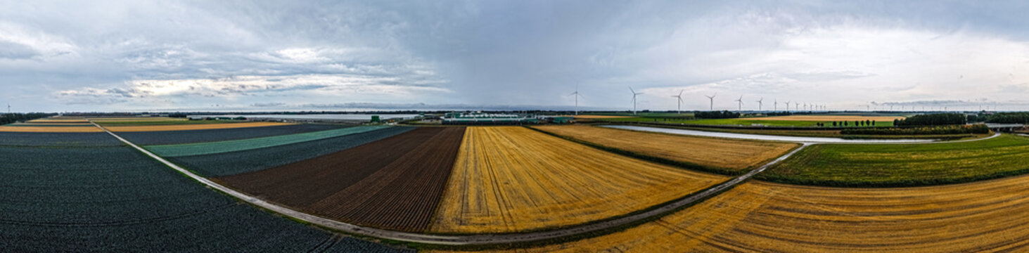 Aerial view of Agriport A7, showcasing vast agricultural fields with diverse crops, wind turbines, and a cloudy sky in Middenmeer, Noord-Holland, Netherlands.