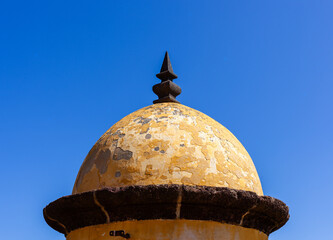 Historic stone turret stands against clear blue sky. Forte de Sao Tiago fortress watchtower in Madeira, Portugal. Coastal defense architecture with weathered dome and spire. © Eugene Ga