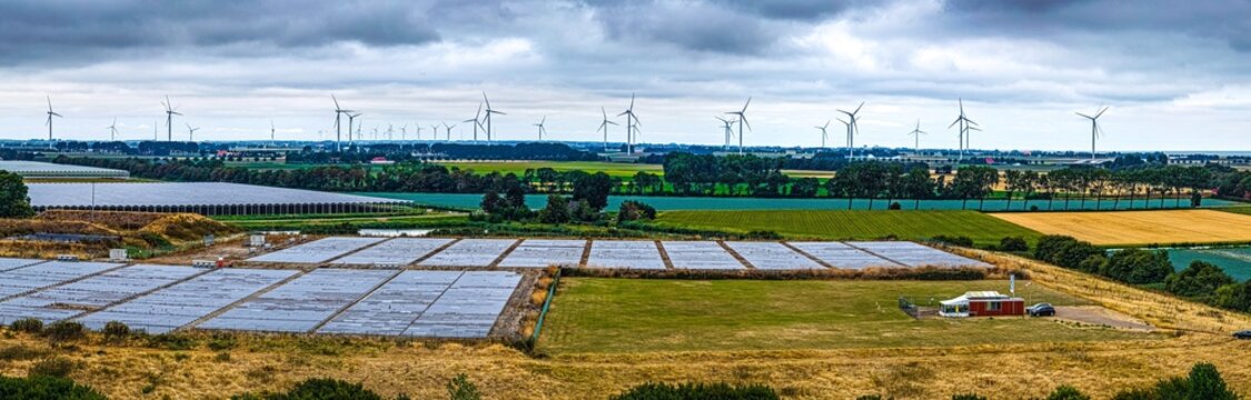 Aerial view of the Agriport A7 industrial area featuring numerous wind turbines, expansive greenhouses, and agricultural fields under a cloudy sky in Middenmeer, Noord-Holland, Netherlands.