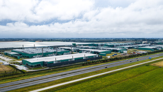 Aerial view of Agriport A7 business park with large industrial warehouses, greenhouses, and solar panels, situated next to a highway in Middenmeer, Noord-Holland, Netherlands.