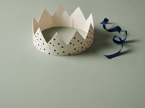 Festive paper party crown with blue polka dots, elegant birthday crown on sage green background, minimalist celebration accessory with curled ribbon