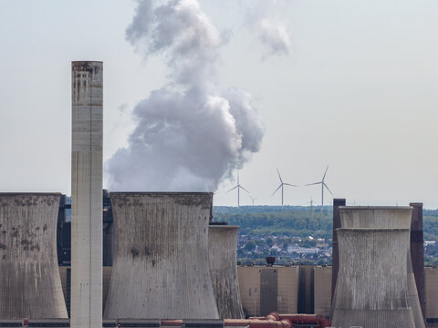 Aerial view of RWE Power AG power plant Niederaussem with cooling towers emitting steam, wind turbines in the background, and industrial infrastructure in Bergheim, Nordrhein-Westfalen, Germany.