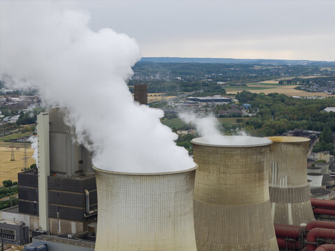 Aerial view of RWE Kraftwerk Weisweiler power plant with large cooling towers emitting steam, surrounded by industrial structures and green landscape in Eschweiler, Nordrhein-Westfalen, Germany.