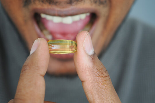 Person holding fish oil capsule between fingers near their open mouth
