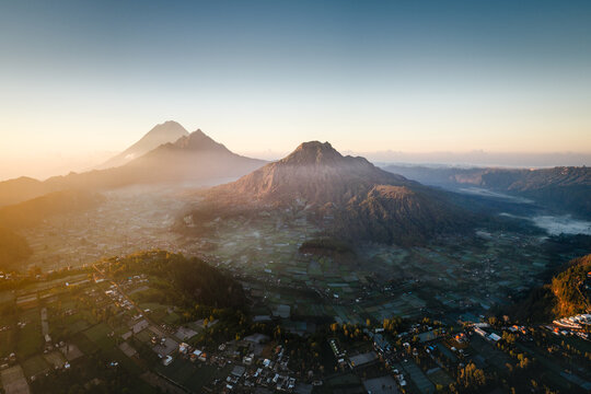 Aerial view of Pinggan village nestled in the valley beneath Mount Batur with terraced fields and morning mist at sunrise in Kintamani, Bali, Indonesia.