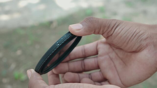 Close up of photographer hand adjusting stop markings on variable neutral density ND filter ring outdoors