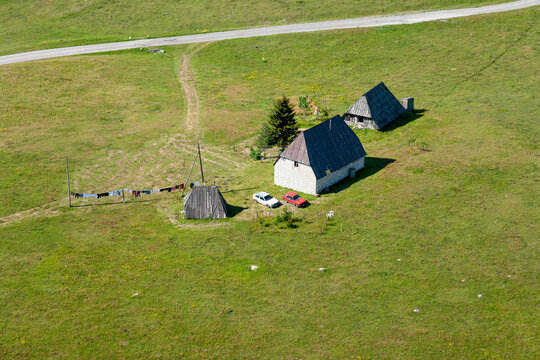 Aerial view of stone houses with steep roofs in the Durmitor region, with parked cars and a clothesline on a green meadow in Zabljak, Zabljak Municipality, Montenegro.
