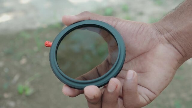 Close up of photographer hand holding circular variable ND filter showing clear optical glass outdoors