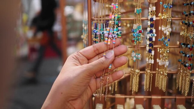 Hand selecting beaded necklaces at a market jewelry display during the day