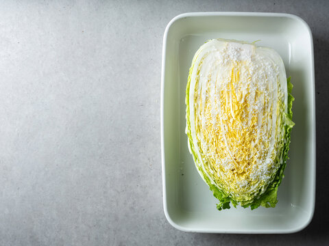 Fresh raw napa cabbage salted with coarse sea salt crystals in a white ceramic tray
