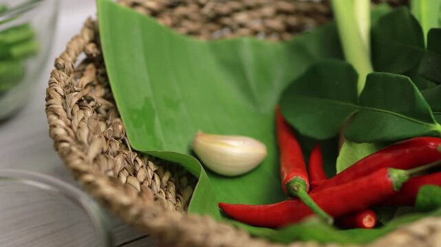 Hand in black glove picking garlic from a basket of Thai herbs