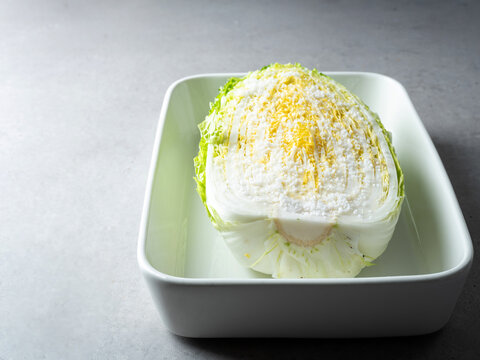 Fresh raw napa cabbage salted with coarse sea salt crystals in a white ceramic tray