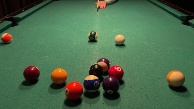 Pool player breaks a rack of billiard balls with white cue ball, balls scatter across the table after opening break shot